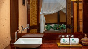 Un baño con lavamanos blanco, un espejo y una cama con mosquitero.