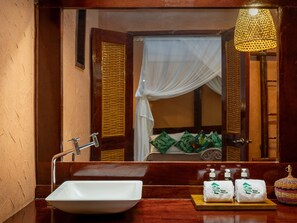 A bathroom with a white sink, a mirror, and a bed with a mosquito net.