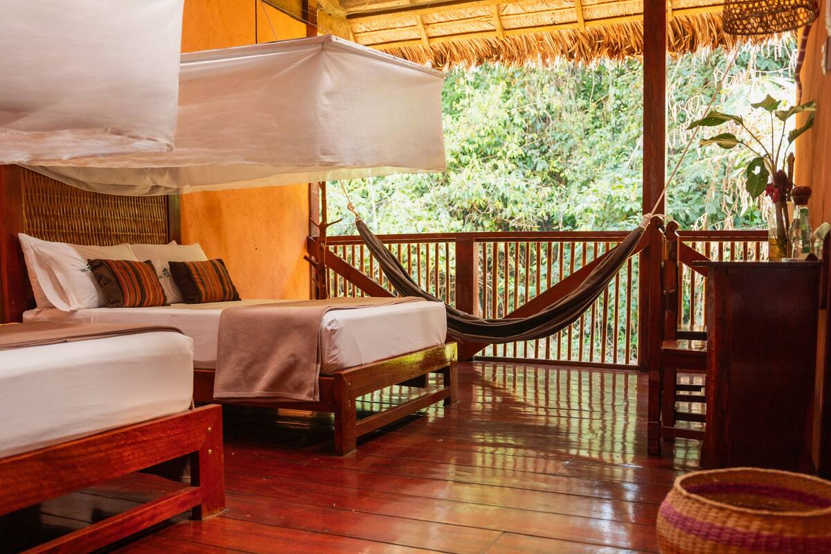 A wooden deck with a hammock, a bed with a canopy, and a view of greenery.