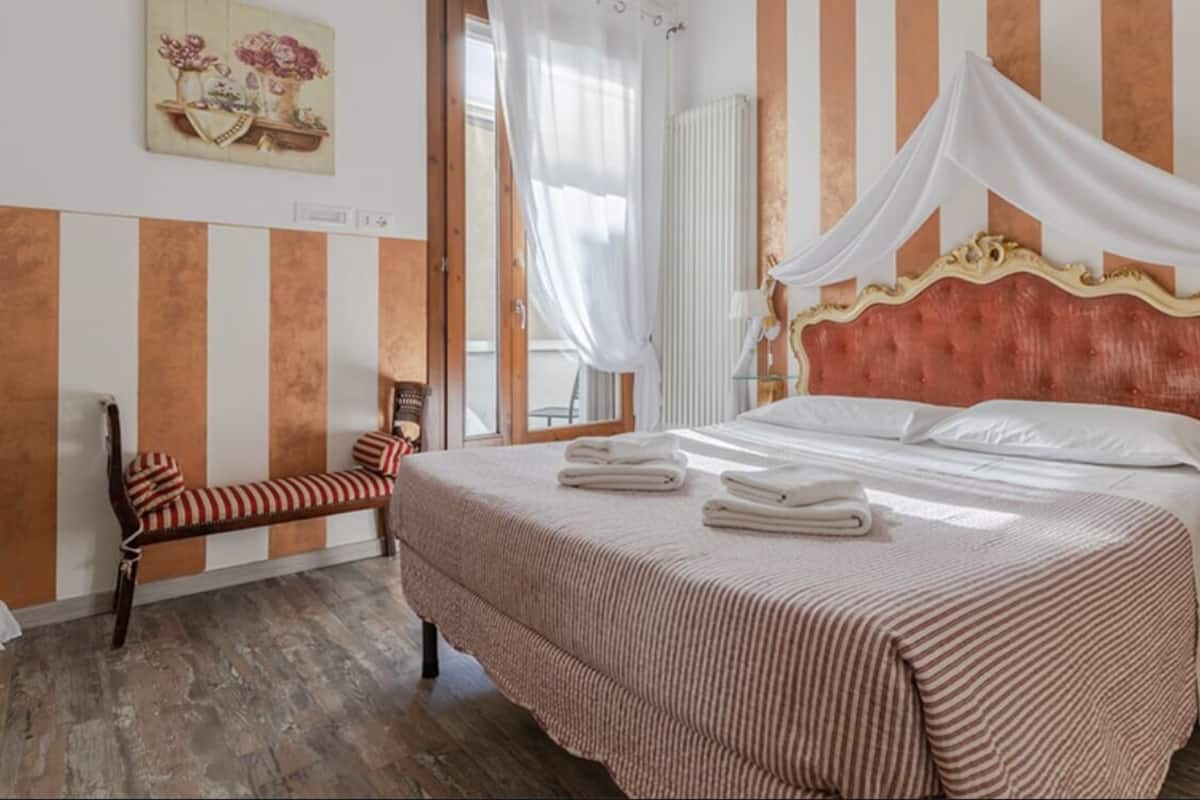 Una habitación de hotel con cama, una silla, una mesita de noche y una ventana con cortinas.