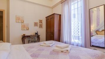 A hotel room with a large bed, a desk with a chair, a wardrobe, and a window with curtains.