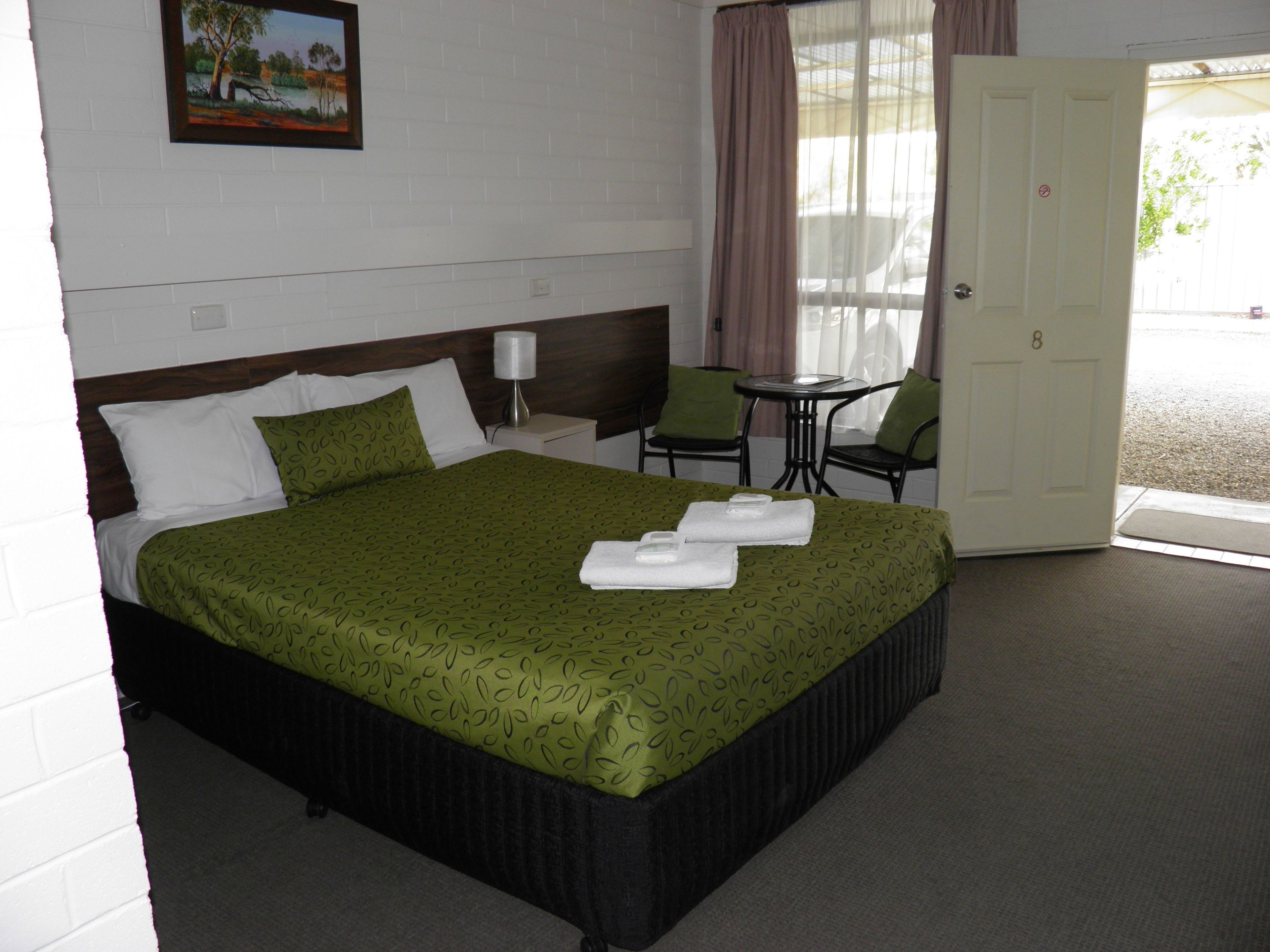 Habitación de hotel con cama, una mesita, dos sillas, una puerta y una ventana con cortinas.