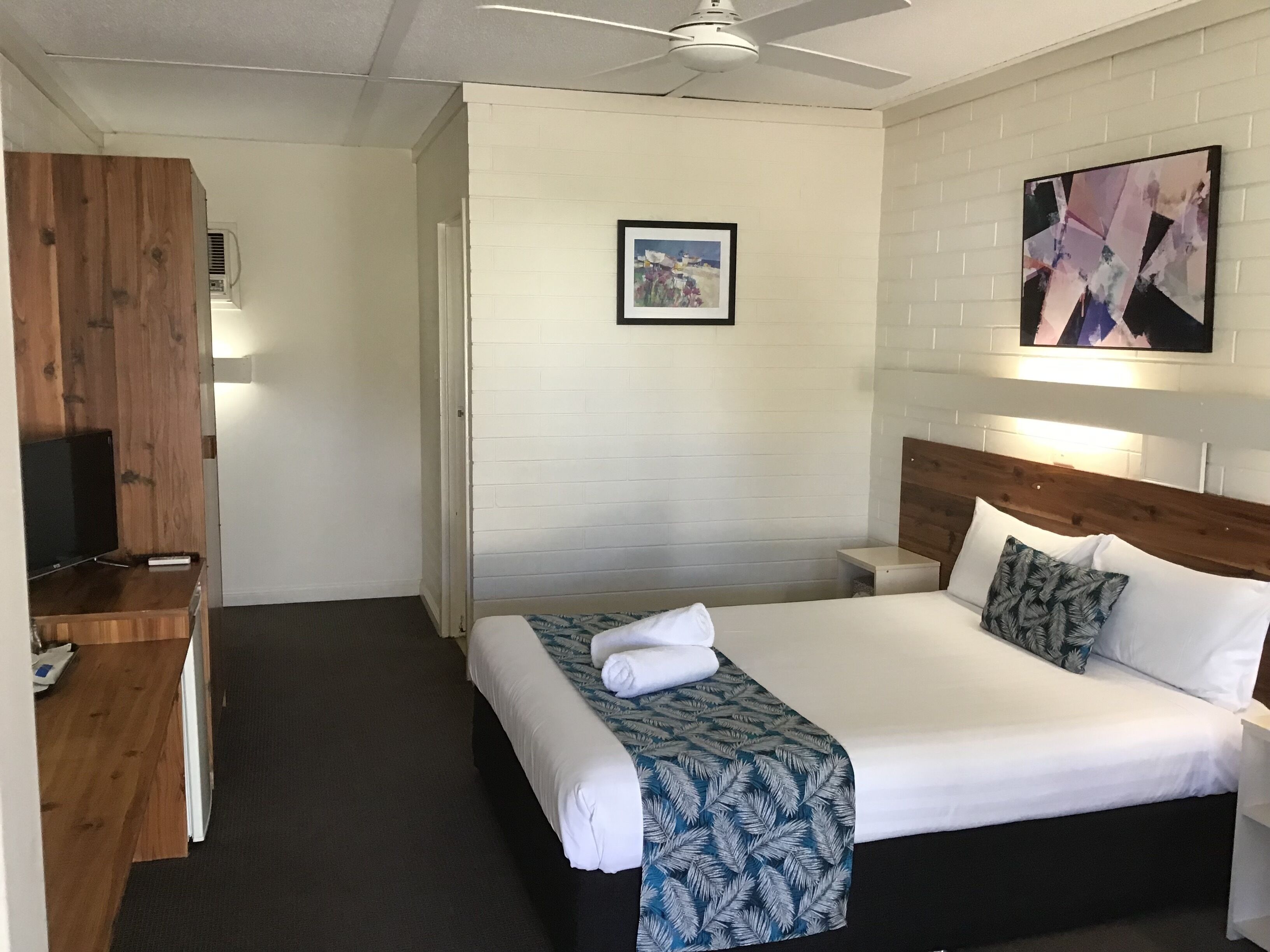 A hotel room with a bed, a desk, a television, a ceiling fan, and a framed picture on the wall.