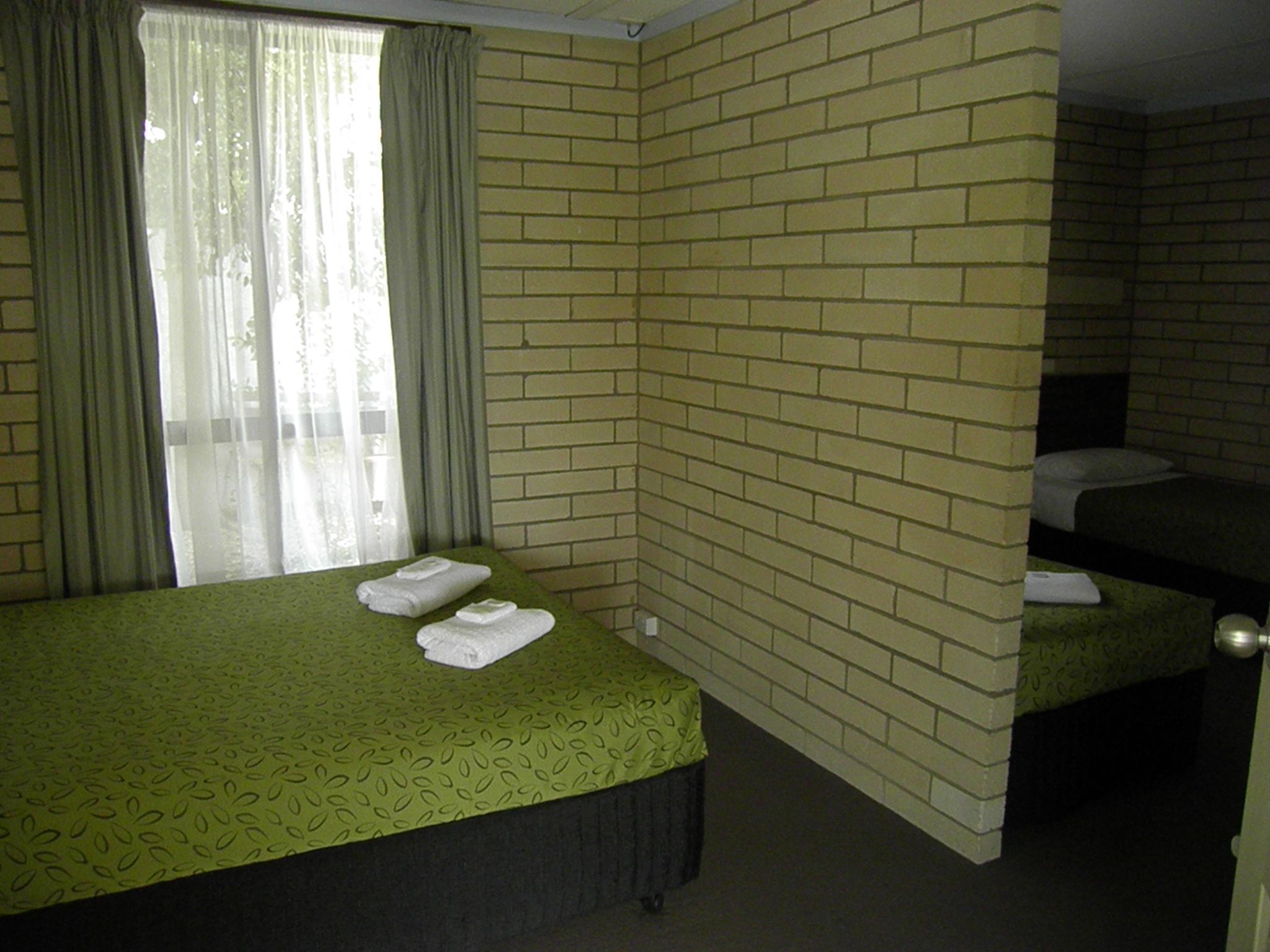 Una camera d'albergo con due letti, una parete con decorazione a mattoni e una finestra con tende.