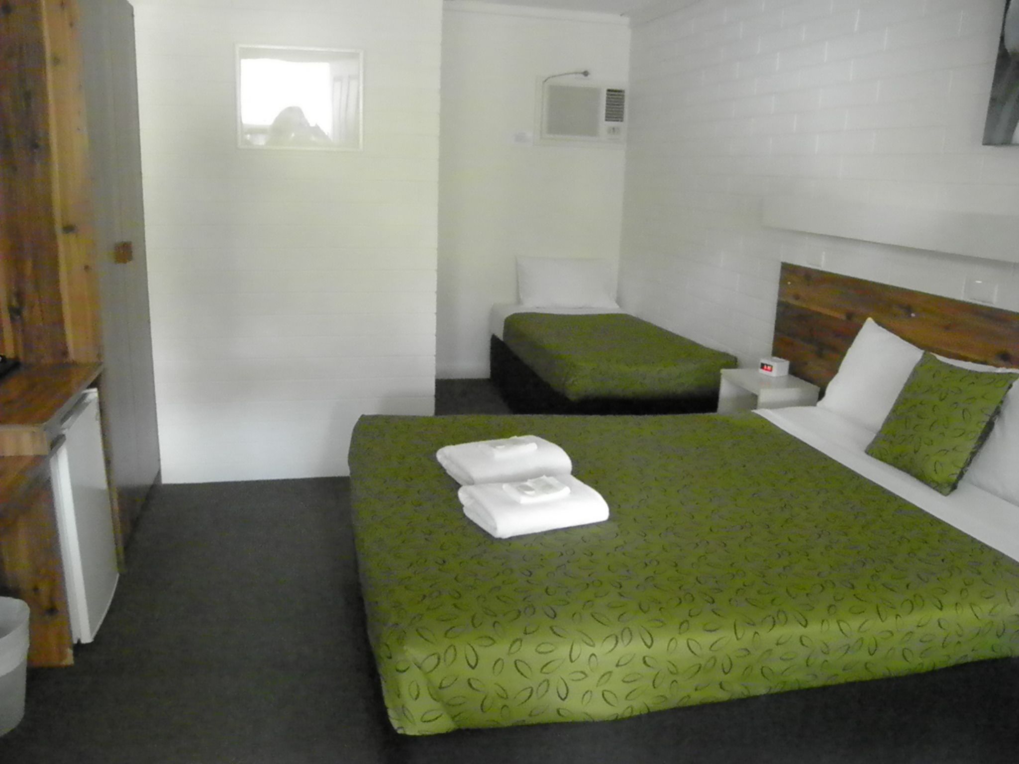 A small, clean room with a single bed, a bedside table, and a window.
