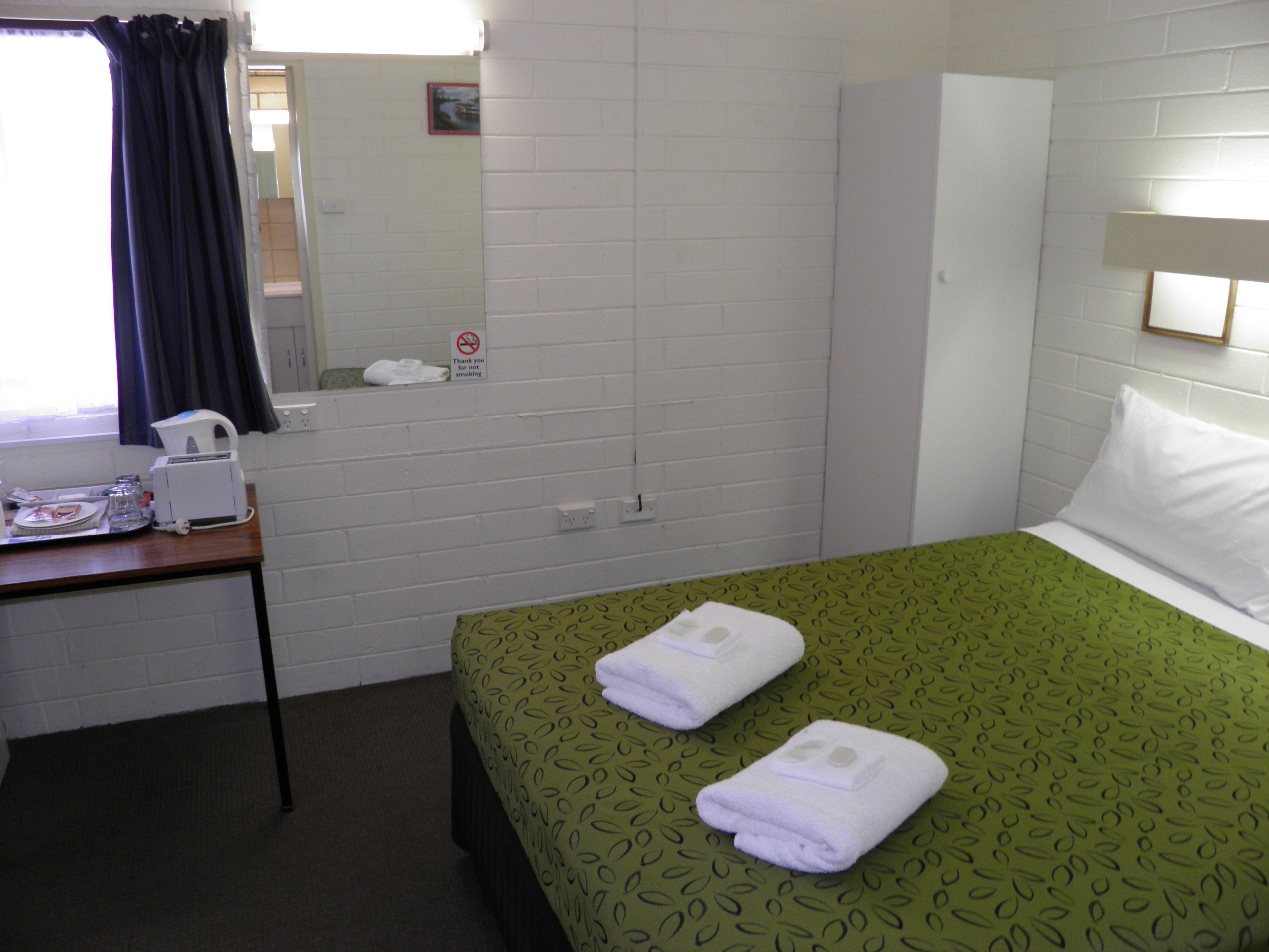 Una habitación de hotel con una cama, un escritorio con cafetera, un espejo y un cartel de 'no fumar' en la pared.