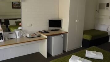 Habitación de hotel compacta con kitchenette, una cama individual, escritorio con ordenador y un refrigerador pequeño.