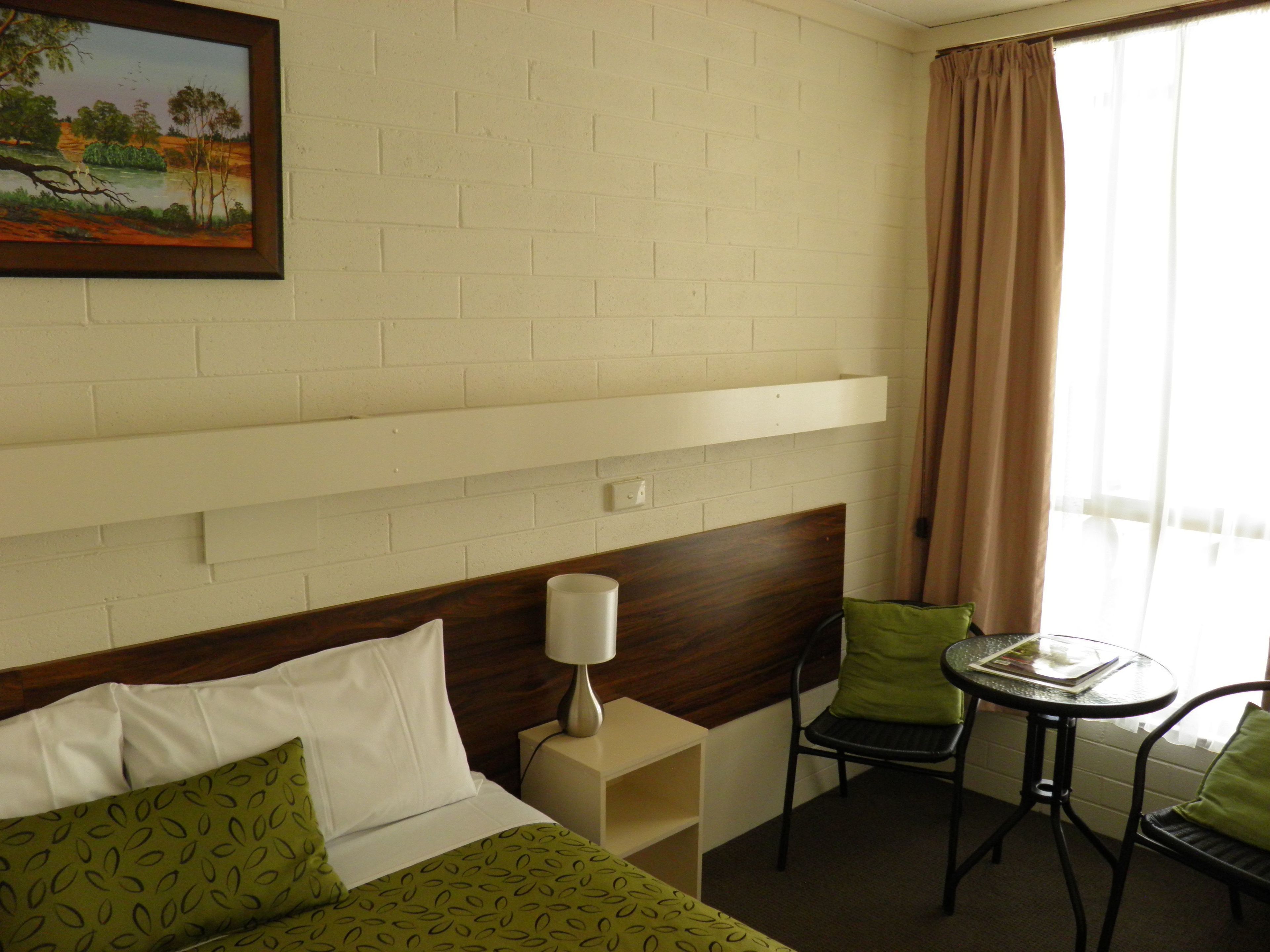 Une chambre d’hôtel avec un lit, un bureau, une chaise, une table et un tableau au mur.