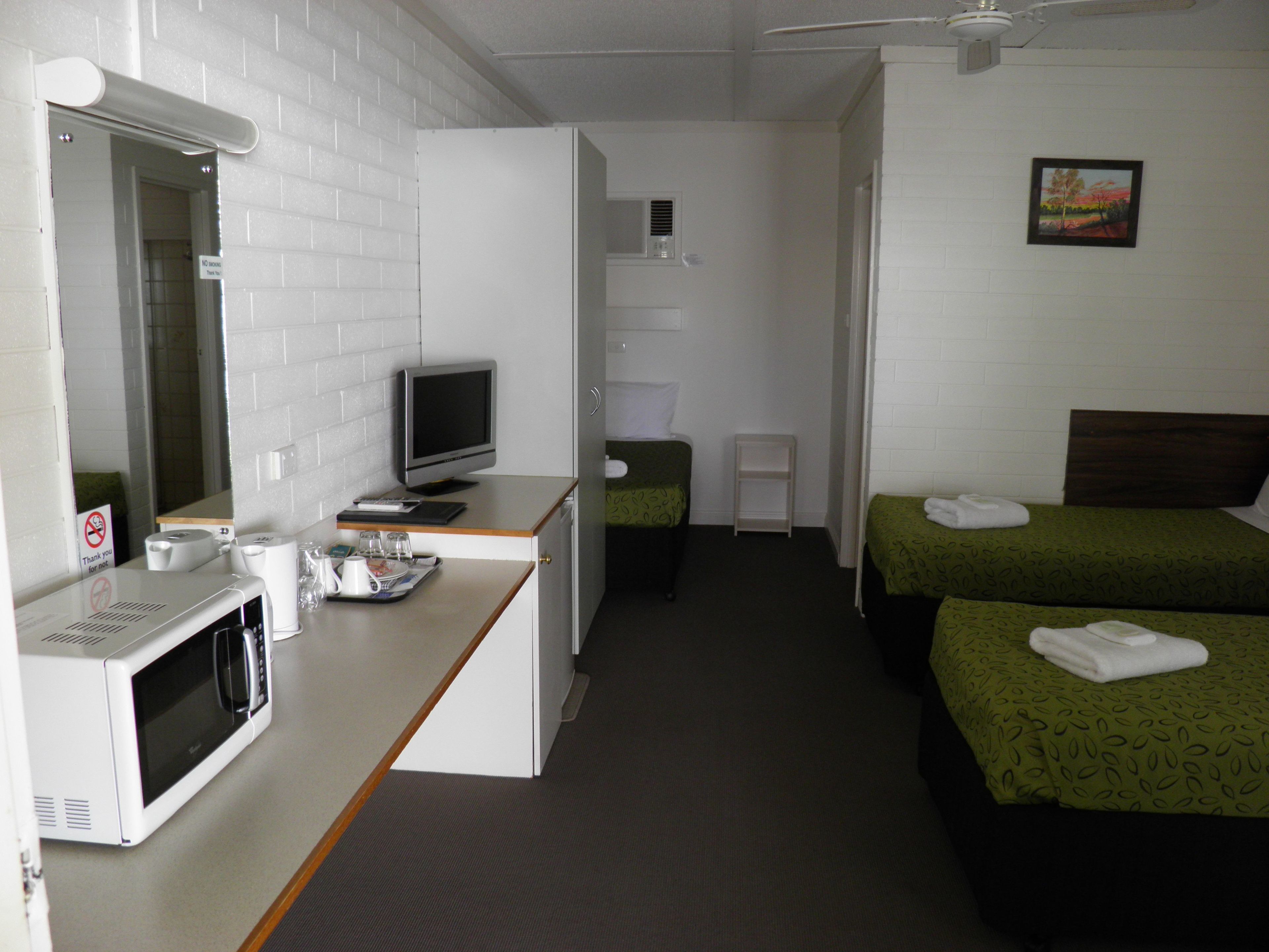 Una habitación de hotel con kitchenette, una cama con ropa de cama verde, una mesita de noche pequeña y un cuadro en la pared.