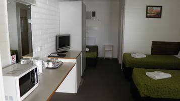 Una habitación de hotel con kitchenette, una cama con ropa de cama verde, una mesita de noche pequeña y un cuadro en la pared.