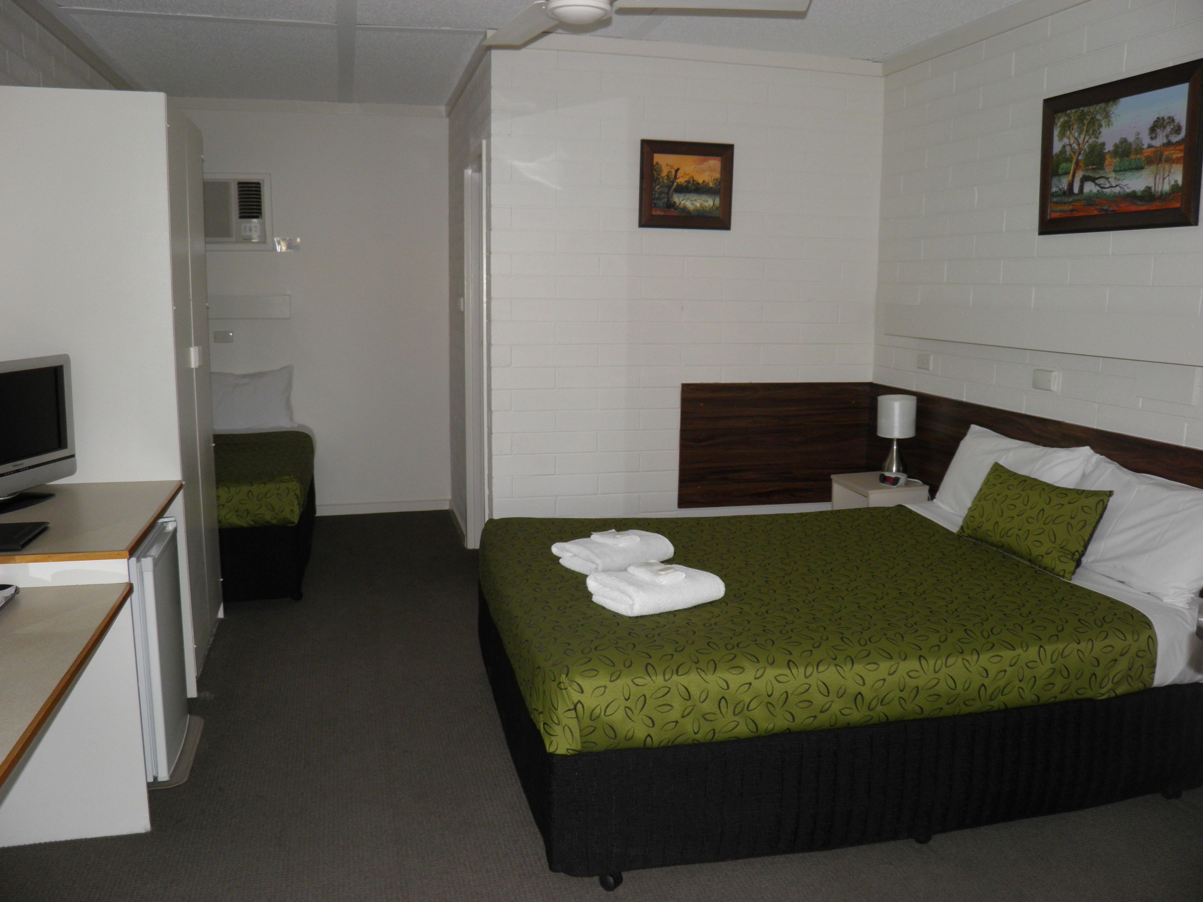 A hotel room with a bed, a desk with a computer, a TV, and a painting on the wall.