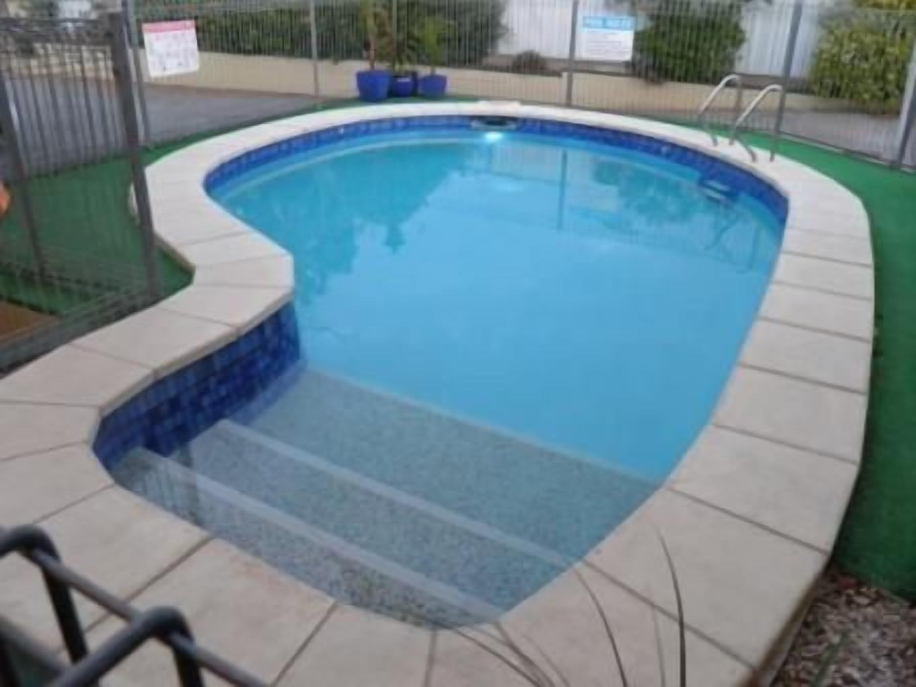 Una piscina con borde curvo, un escalón pequeño para entrar al agua y una escalera de metal.