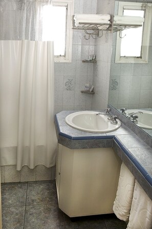 A bathroom with a corner sink, a shower, and a mirror.