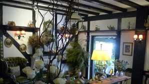 Una stanza accogliente con soffitto in legno, un grande vaso con fiori, un tavolo con una lampada e una sedia.