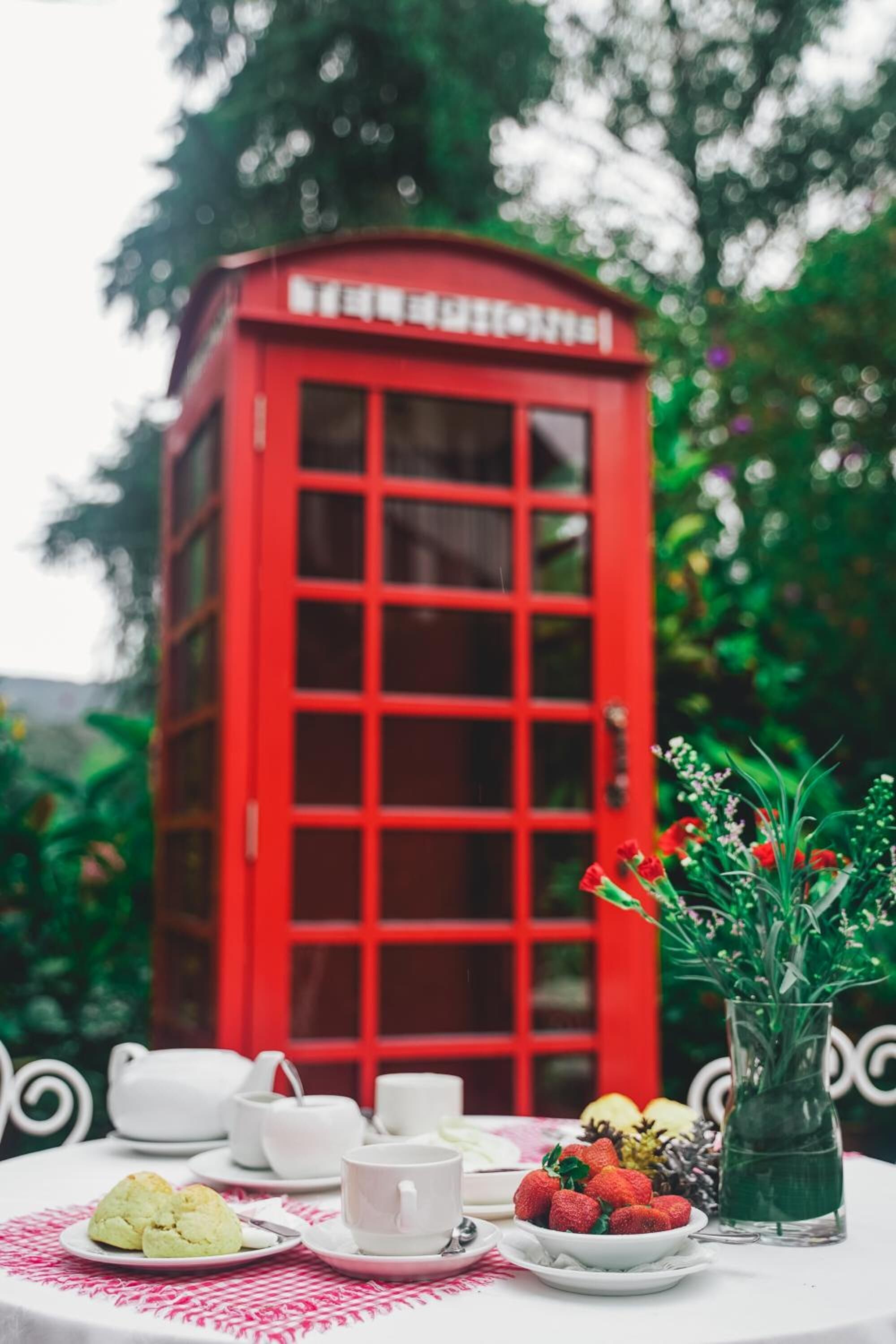 A red telephone booth with a table set for tea, including cups, teapots, and pastries.