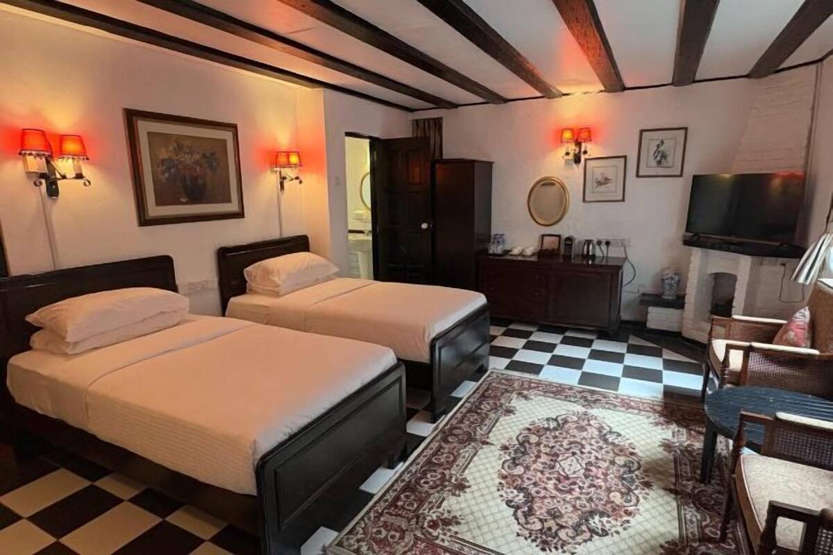Ein Hotelzimmer mit zwei Betten, einem Schachbrettfußboden, einem gemusterten Teppich, einem Schreibtisch mit Stühlen, einem Fernseher und Wandleuchten.