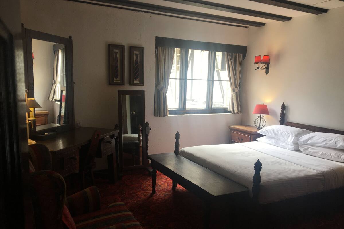 Ein Hotelzimmer mit einem großen Bett, einem Schreibtisch, einem Stuhl, einem Spiegel und einem Fenster mit Vorhängen.