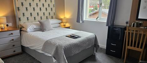 A neatly arranged bedroom with a bed, bedside lamps, a small desk, and a window with a view of buildings.