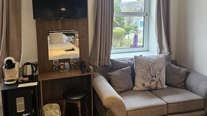 Een gezellige woonkamer met een flatscreen televisie aan de muur, een houten bureau met een koffiezetapparaat en een comfortabele bank met decoratieve kussens.