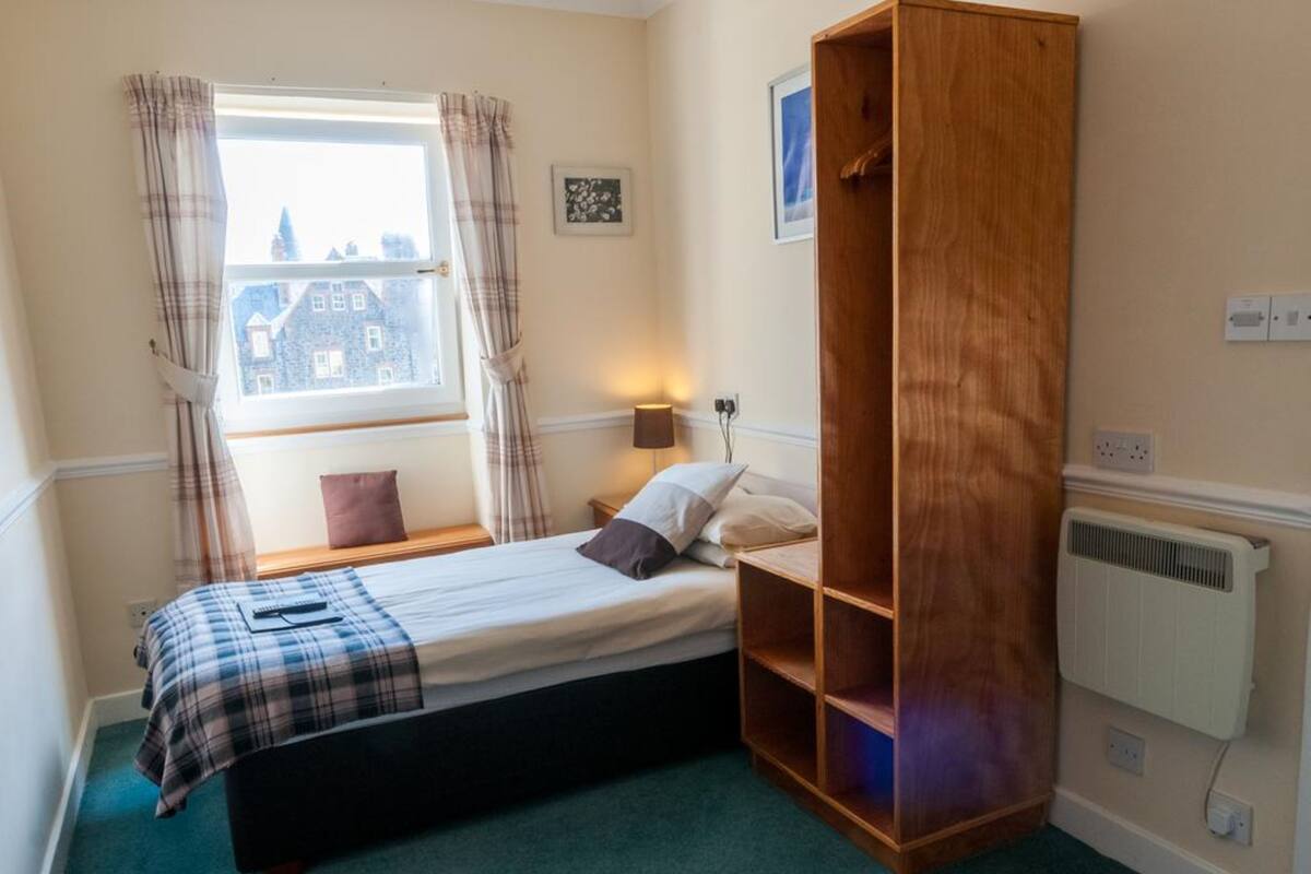 Ein Schlafzimmer mit einem Bett, einem Holzschrank, einem Fenster mit Vorhängen, einer Nachttischlampe und einer Heizung.