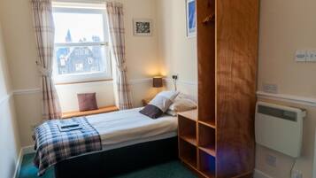 A bedroom with a bed, a wooden wardrobe, a window with curtains, a bedside lamp, and a radiator.