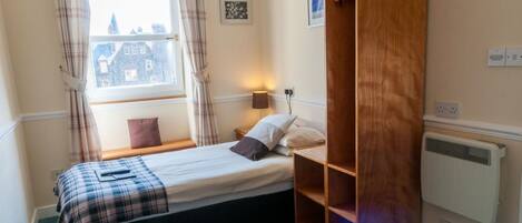 A bedroom with a bed, a wooden wardrobe, a window with curtains, a bedside lamp, and a radiator.