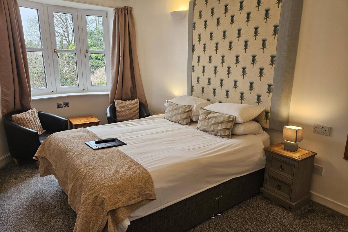 Ein Schlafzimmer mit einem Bett, einem Sessel, einem Nachttisch und einem Fenster mit Vorhängen.