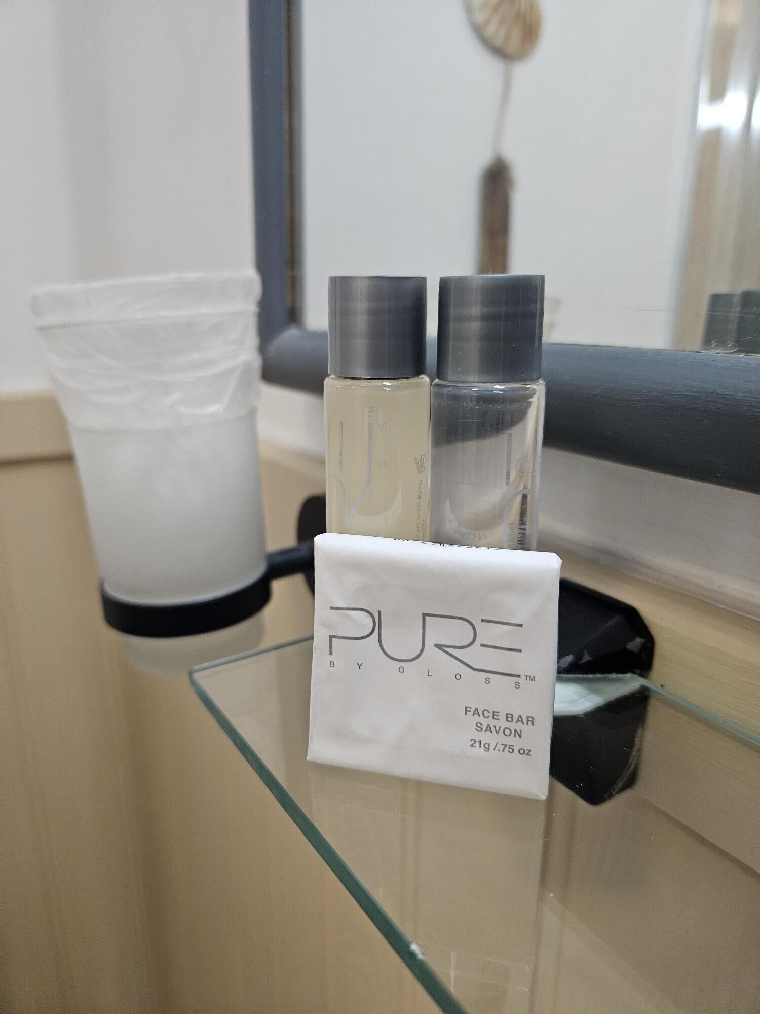 A bathroom counter with a glass container, two bottles, and a white packet labeled "PURE BY GLOSS".