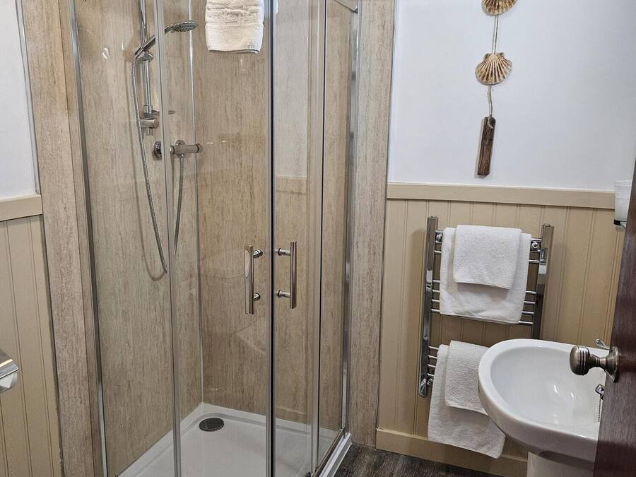 A modern bathroom with a glass-enclosed shower, a wooden floor, a white sink, and a towel rack with multiple towels.