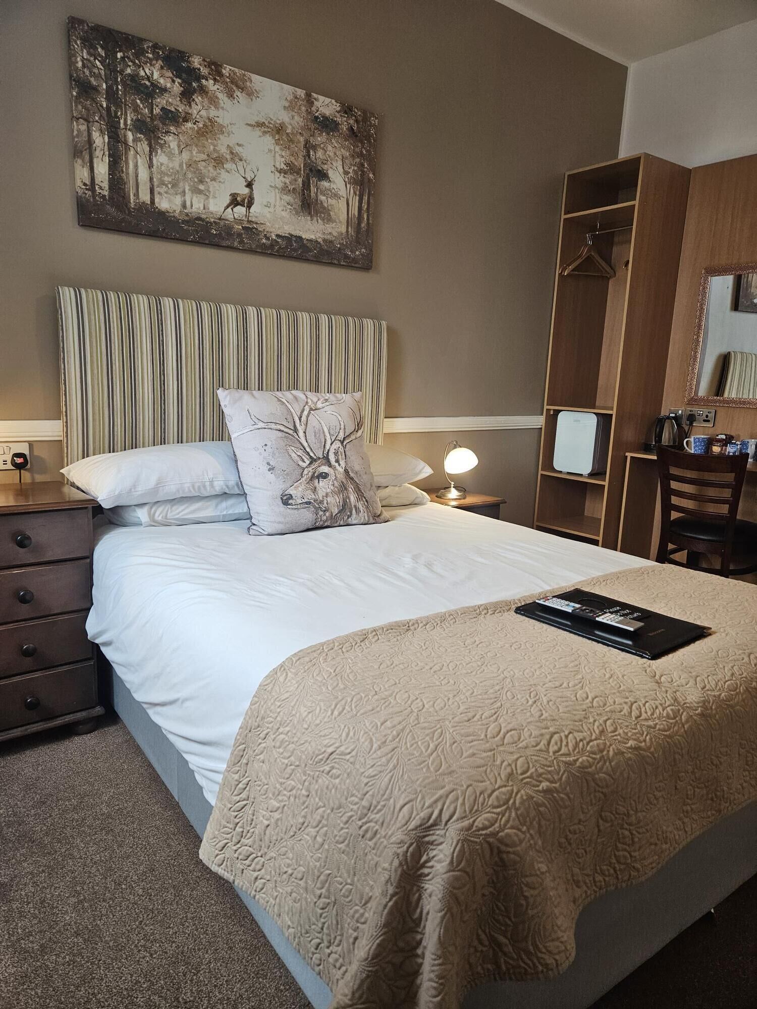 A neatly arranged bedroom with a large bed, a bedside table, a lamp, a wardrobe, and a painting on the wall.