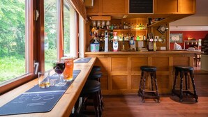 Een bar met houten barstoelen, een toonbank met diverse flessen en een tappunt, en een menukaart op een schoolbord.