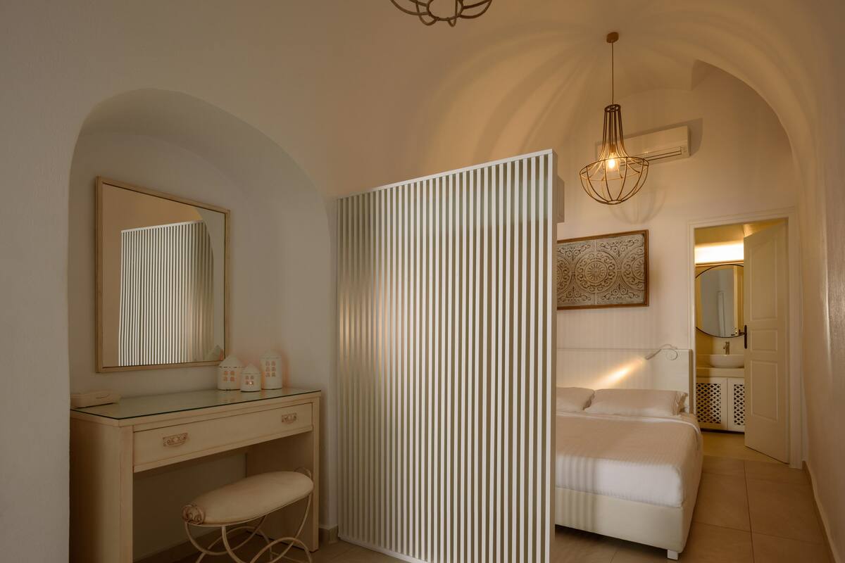 A bedroom with a bed, a bedside table, a mirror, and a hanging light fixture.