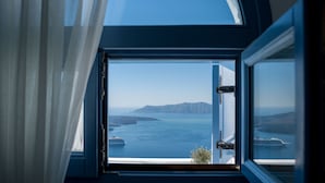 A room with a large window offering a view of the sea and distant land. - Kamares Apartments (Santorini)