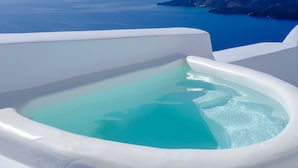 A white bathtub with clear blue water, overlooking a coastal landscape with distant islands and cliffs. - Kamares Apartments (Santorini)