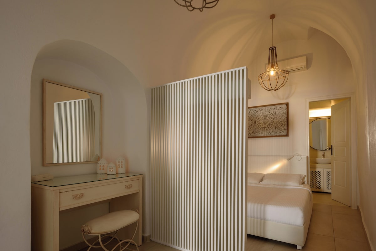 Un dormitorio con cama, mesita de noche, espejo y lámpara colgante.