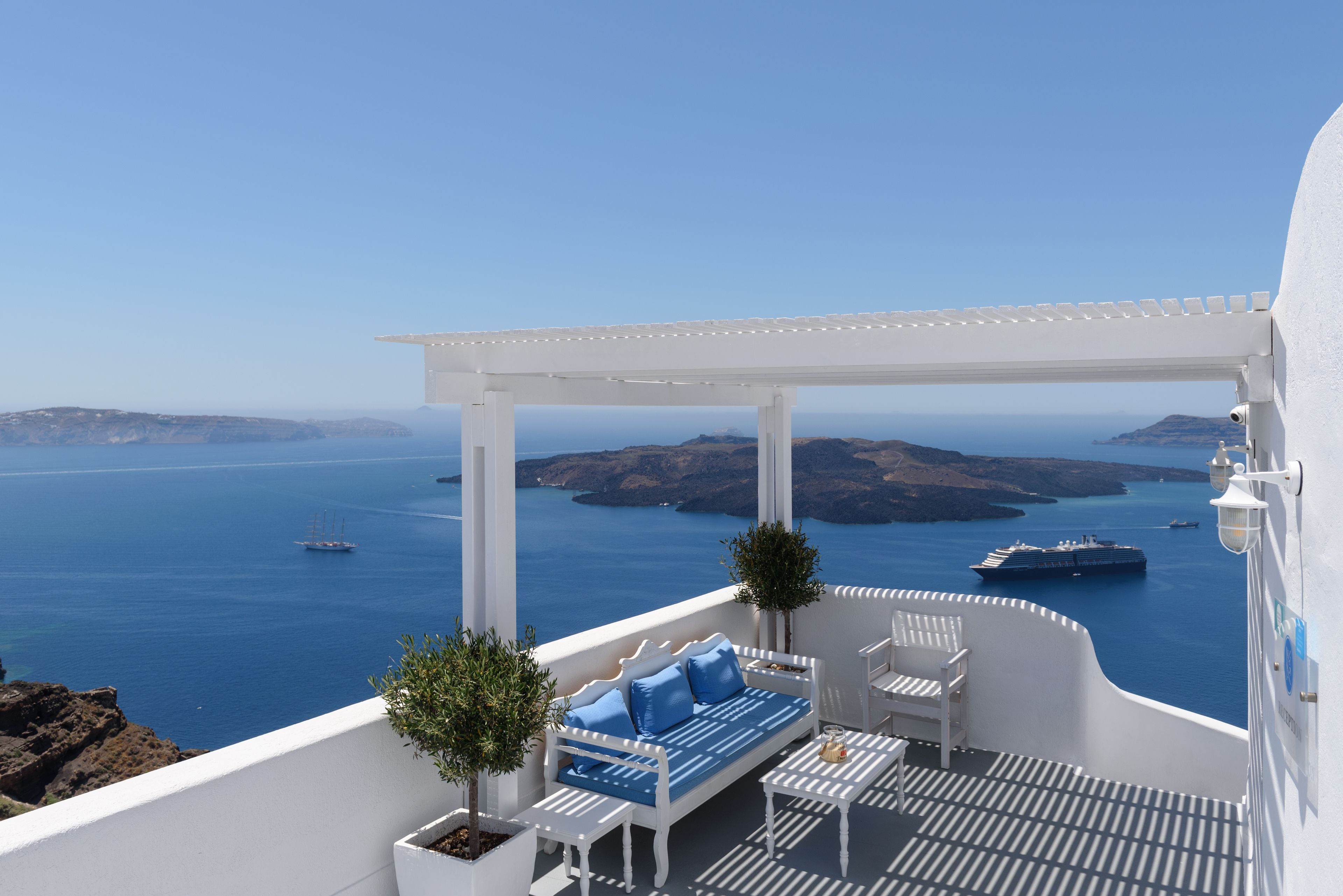 A white outdoor seating area with a view of the sea and islands.