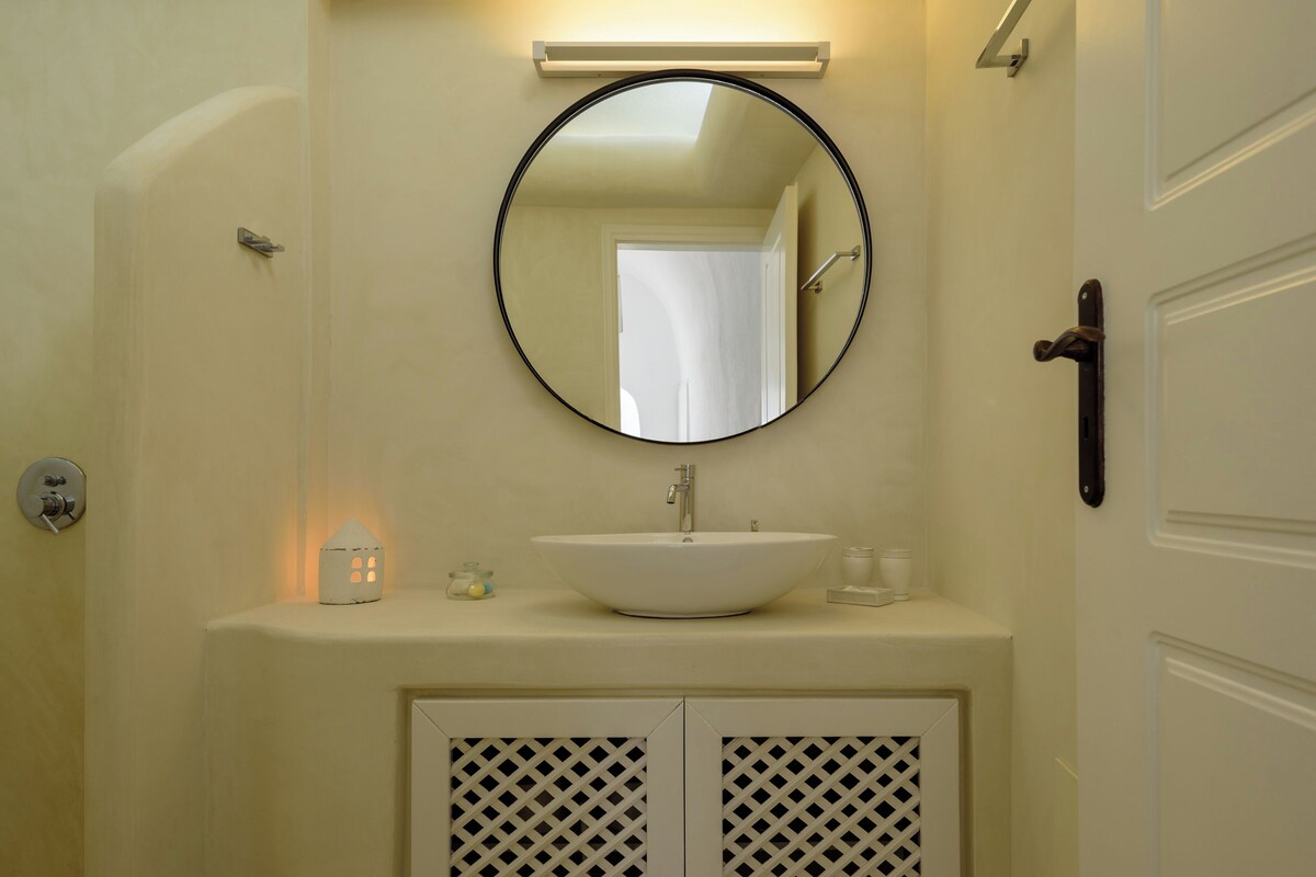 Un baño con un espejo redondo, un lavabo blanco y una puerta con pomo.