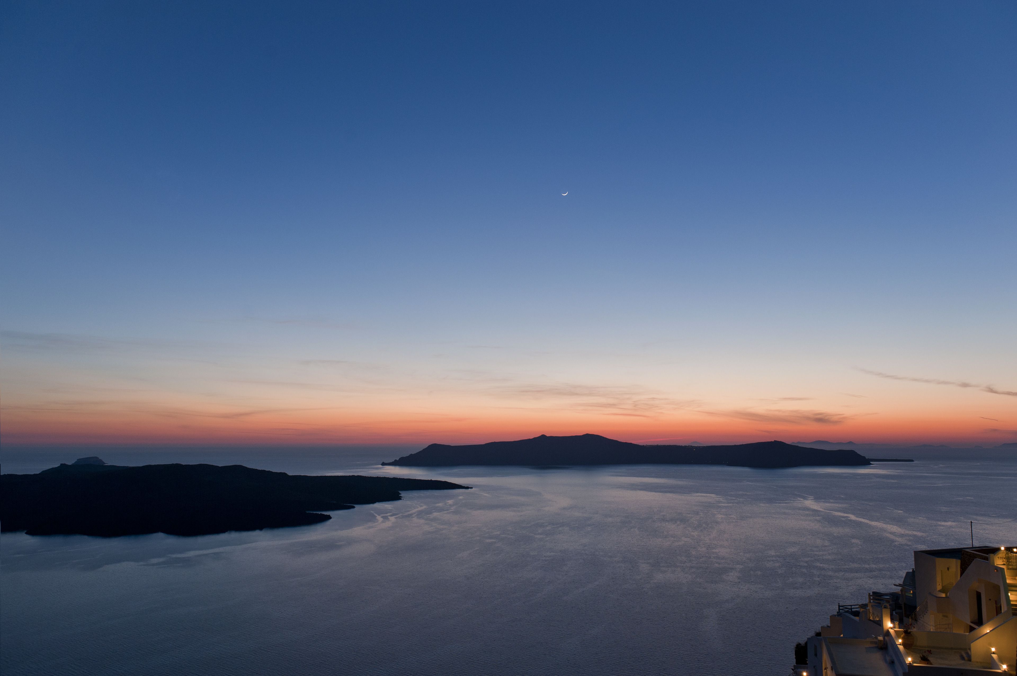 Vista costera con cielo despejado, luna distante y mar tranquilo.