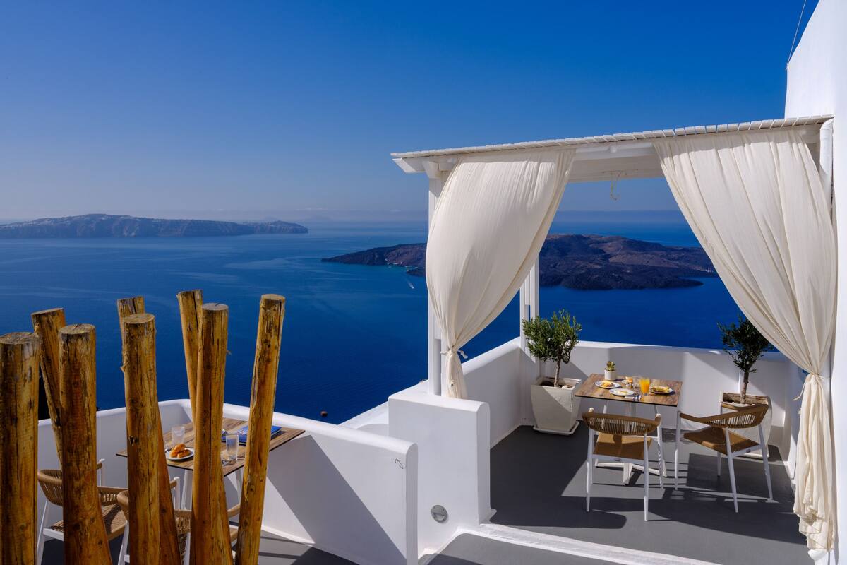 A terrace with a table and chairs, overlooking a scenic view of the sea and islands.