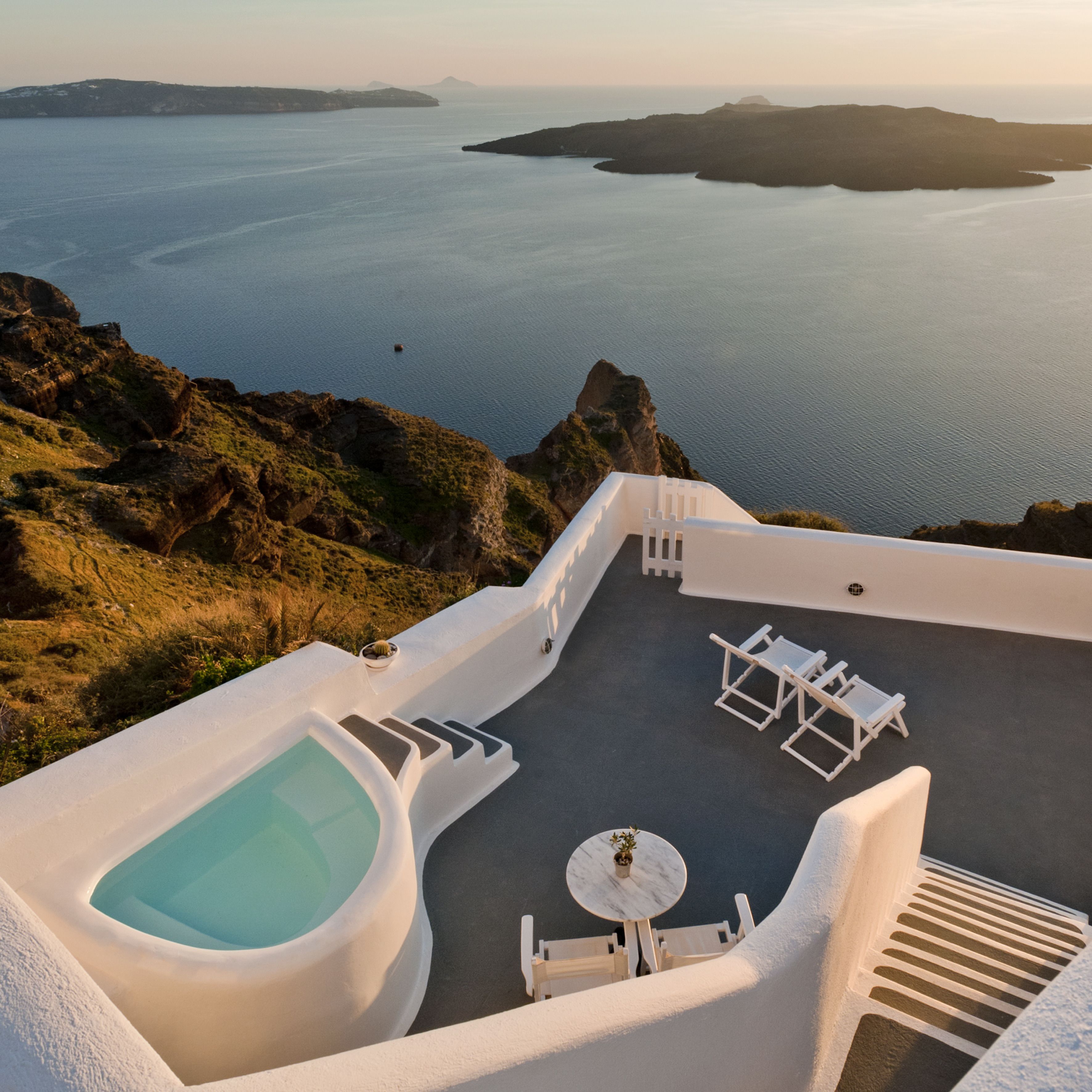 Une terrasse sur le toit dotée d’un jacuzzi, de chaises longues et d’une table, offrant une vue sur un paysage côtier avec des falaises et la mer.