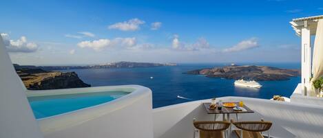 A terrace with a table set for two, overlooking a sea view with a yacht and distant islands.