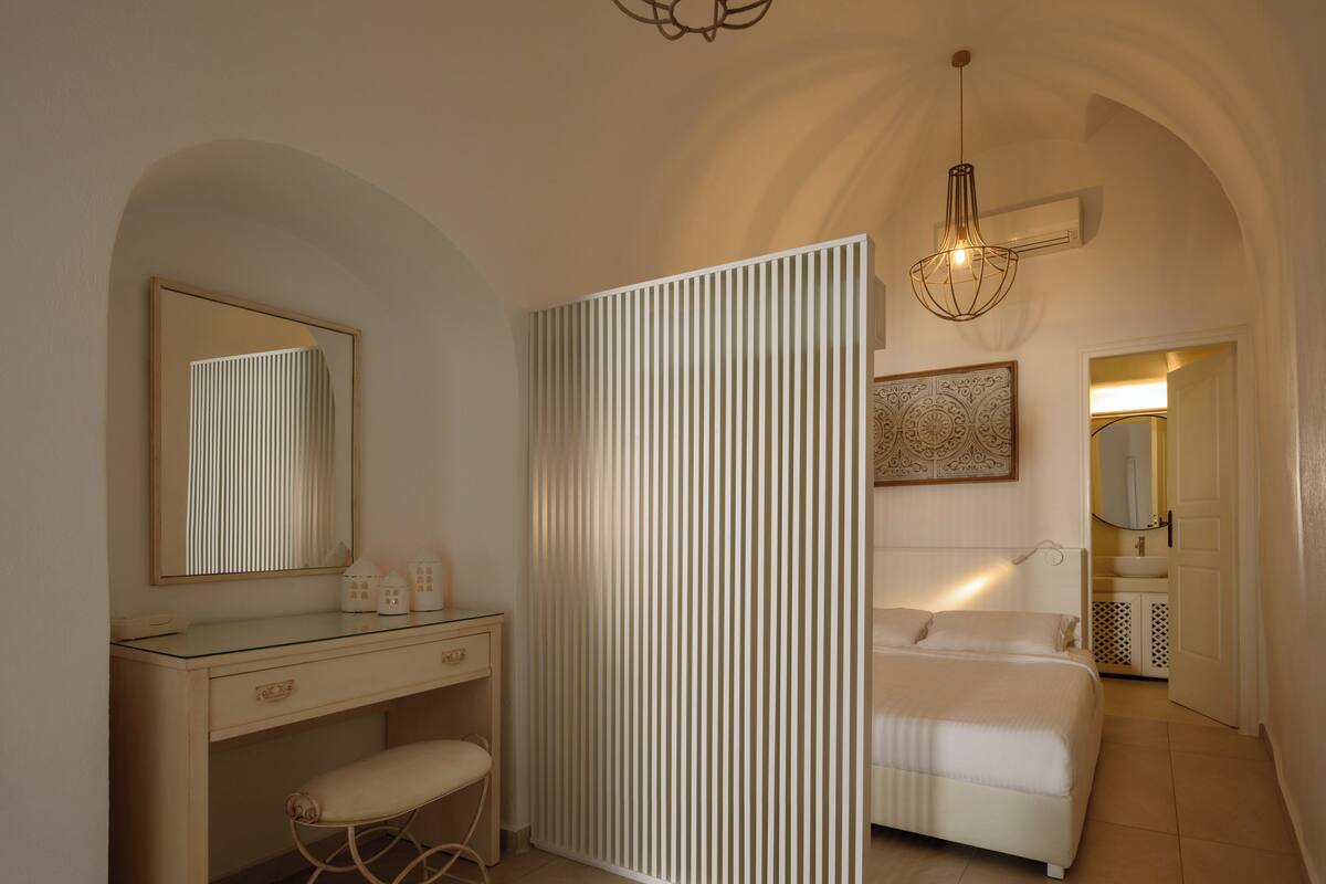 A bedroom with a bed, a bedside table, a mirror, and a hanging light fixture.