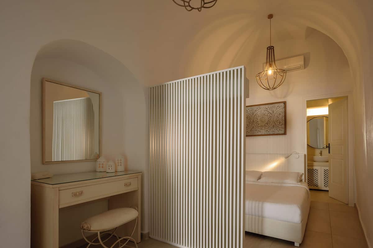 A bedroom with a bed, a bedside table, a mirror, and a hanging light fixture.