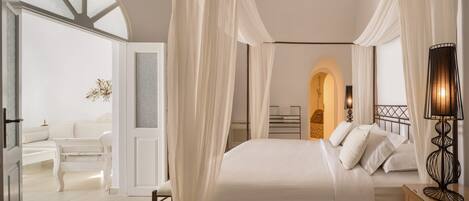 A bedroom with a large bed, a bedside table with a lamp, and a view of a bathroom through an archway.