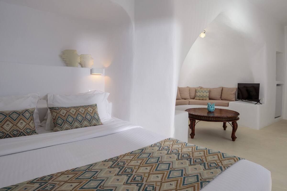 A modern, minimalist hotel room with a large bed, a sofa, a coffee table, and a television.