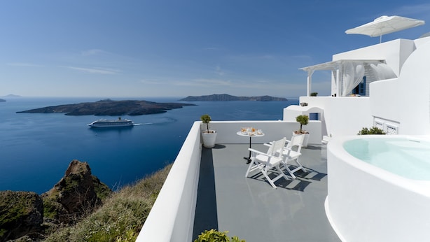 A modern white building with a pool, outdoor seating, and a view of the sea and islands. - Kamares Apartments (Santorini)
