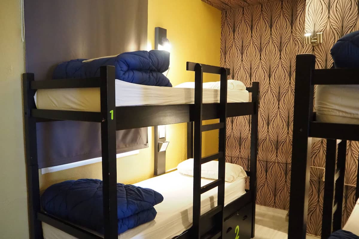 Habitación con literas, dos camas, cada una con almohada y manta. Hay una luz montada en la pared y una cortina estampada.