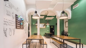 Un comedor con mesas y bancos de madera, paredes verdes y arcos blancos.