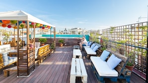 Una terraza en la azotea con bancos de madera, un espacio de estar cubierto y plantas en macetas.