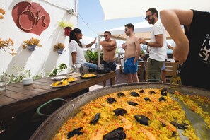 A large communal dining table with a seafood paella dish in the foreground.
